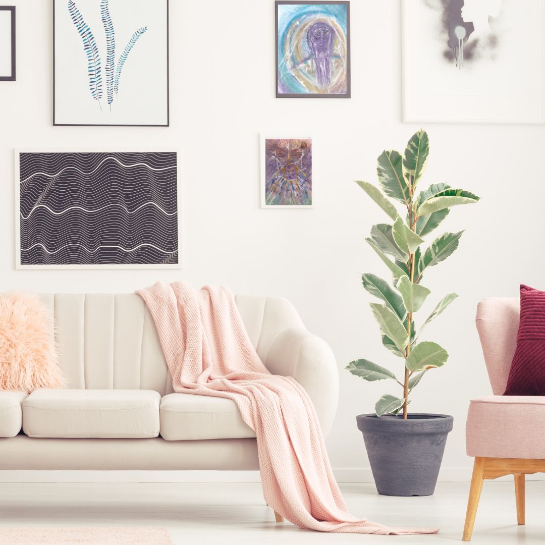 Ajuji, a whimsical Lyran star being with cat-like features, framed as part of a gallery wall above a sofa with a pink throw blanket.