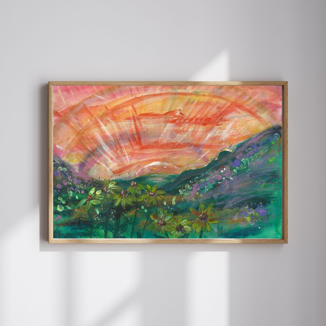 An A3 painting of a peaceful female figure lying in a hilly grassy landscape with yellow flowers, during sunset. The artwork features warm tones of orange, yellow, and green. The piece is framed in a thin wooden frame.