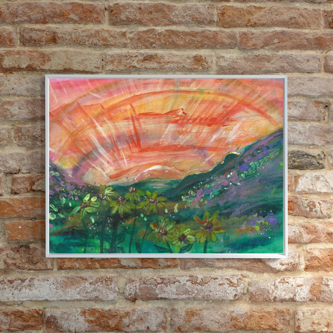 A photo of the A3 painting framed in a white frame, displayed on a stone wall. The artwork features a peaceful female figure lying in a hilly grassy landscape with yellow flowers, during sunset, with warm orange, yellow, and green tones.
