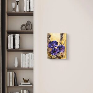 A canvas painting on a warm beige wall next to a styled bookcase, depicting deep purple anemones on a golden-brown background.